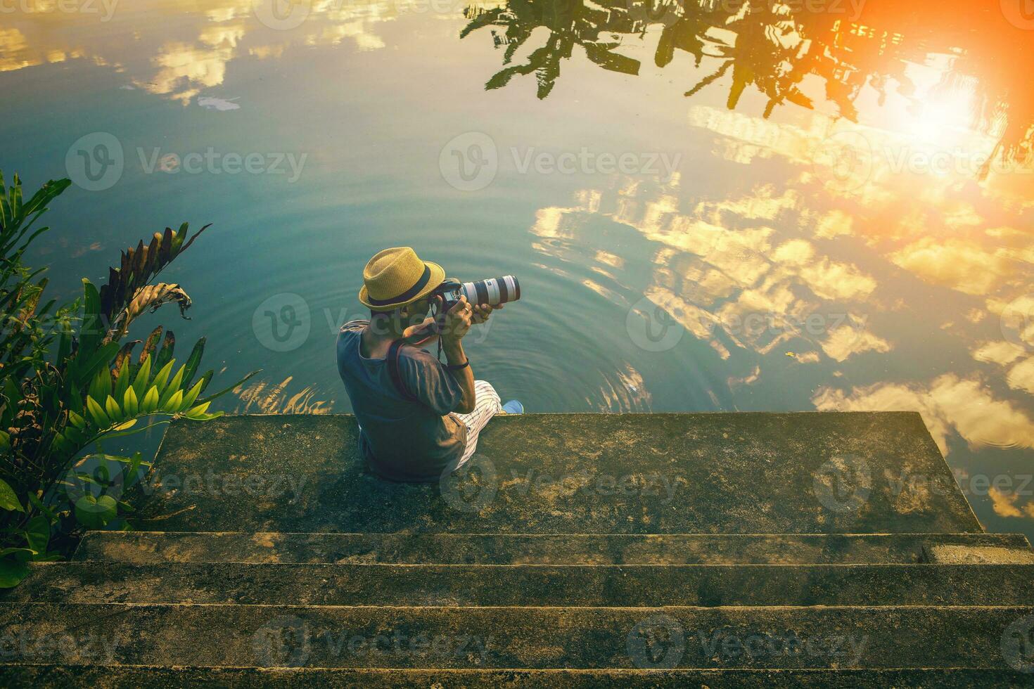 hipster man taking a photograph on pier against beautiful skies reflect on lake photo