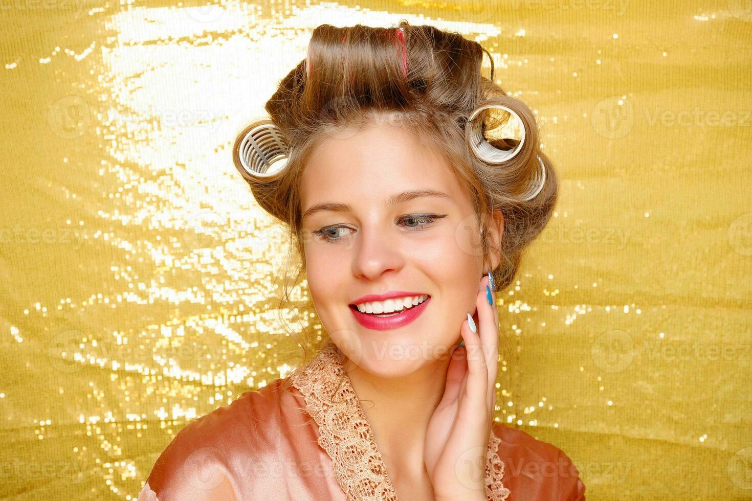 Beautiful girl in hair curlers isolated on gold photo