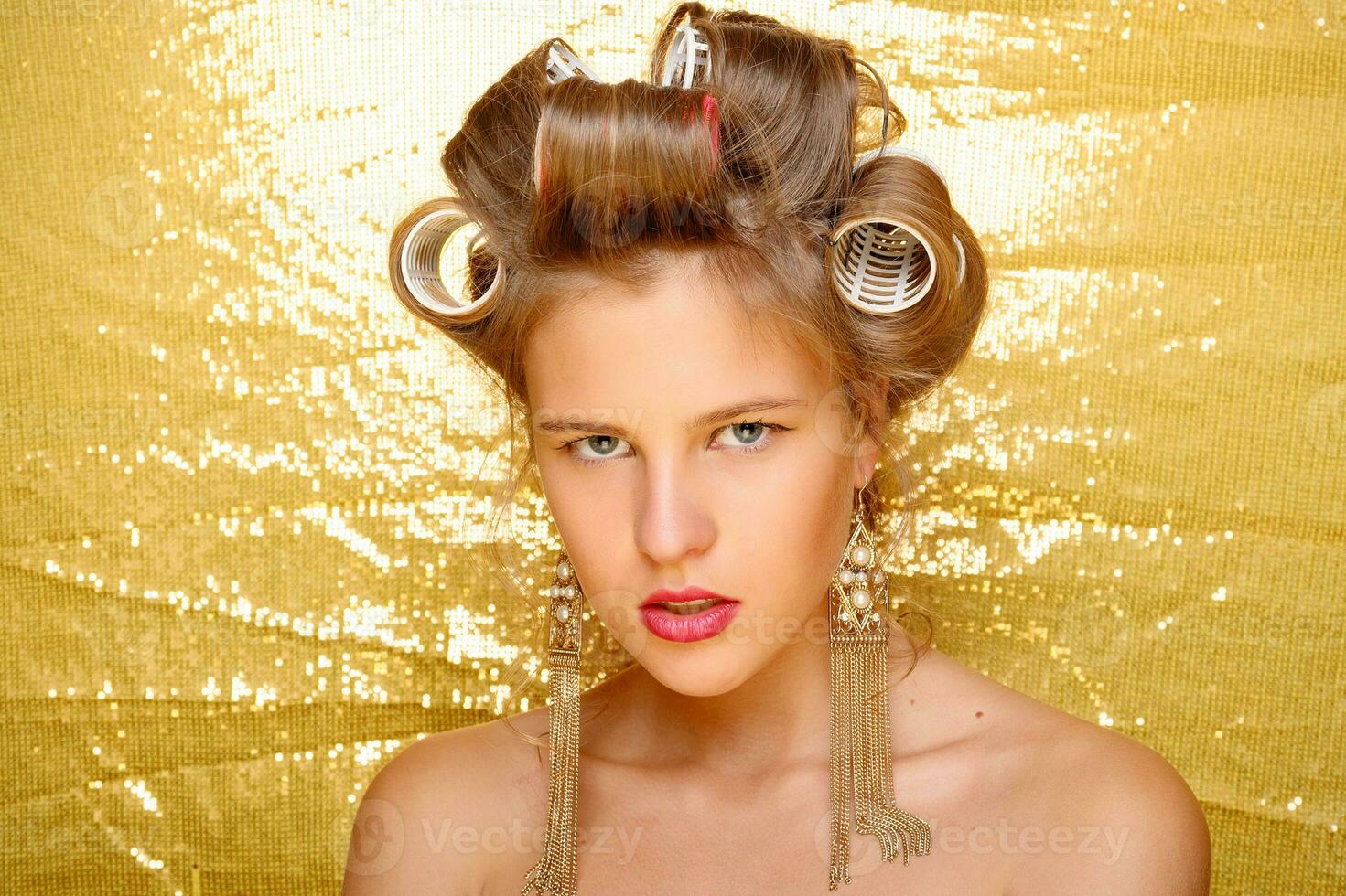 Beautiful girl in hair curlers isolated on gold photo