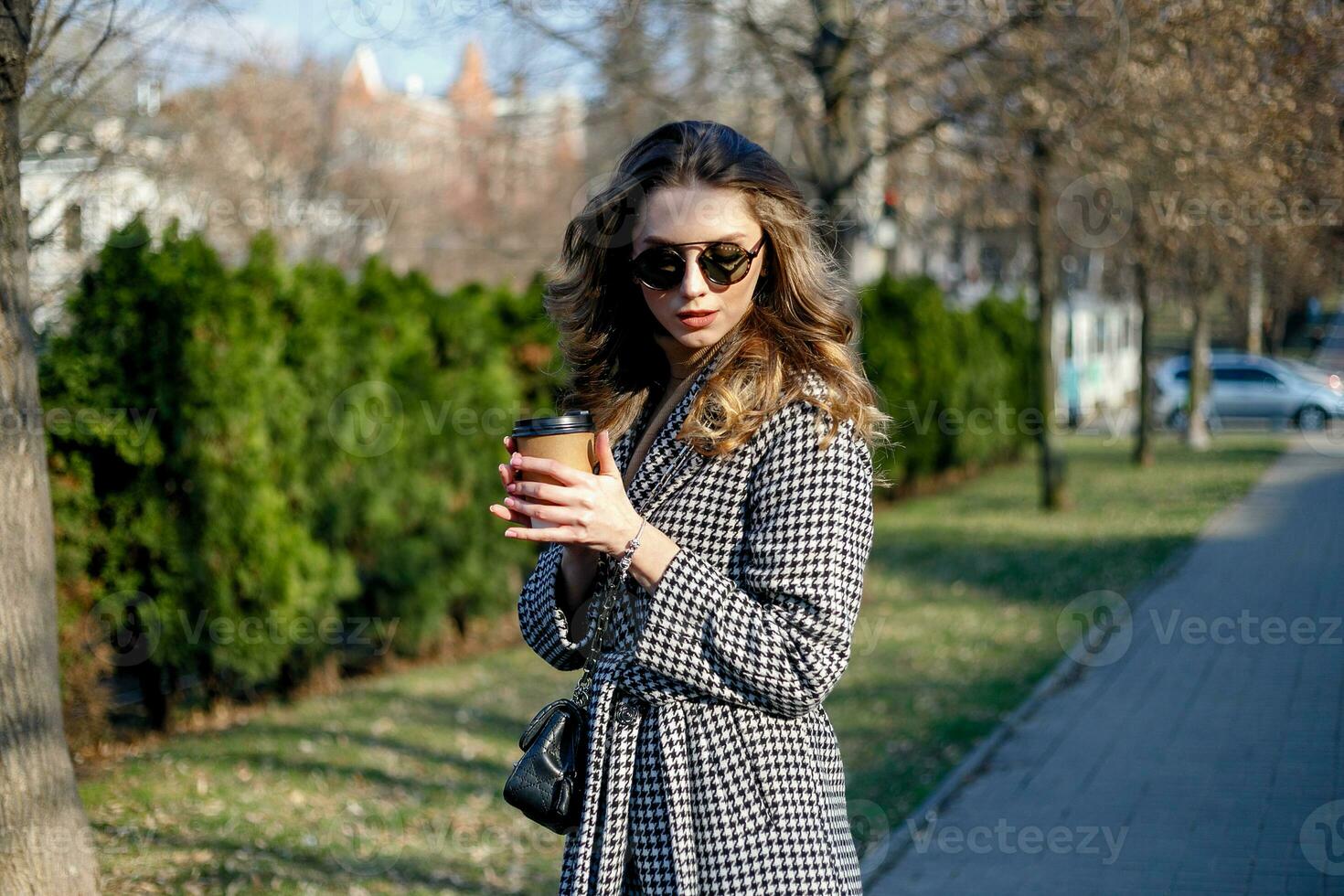 woman in trench coat walking and drinking coffee from paper cup photo