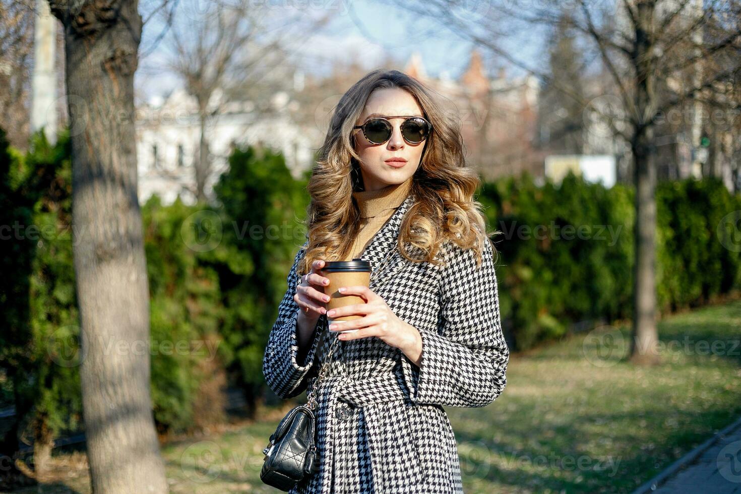 woman in trench coat walking and drinking coffee from paper cup photo