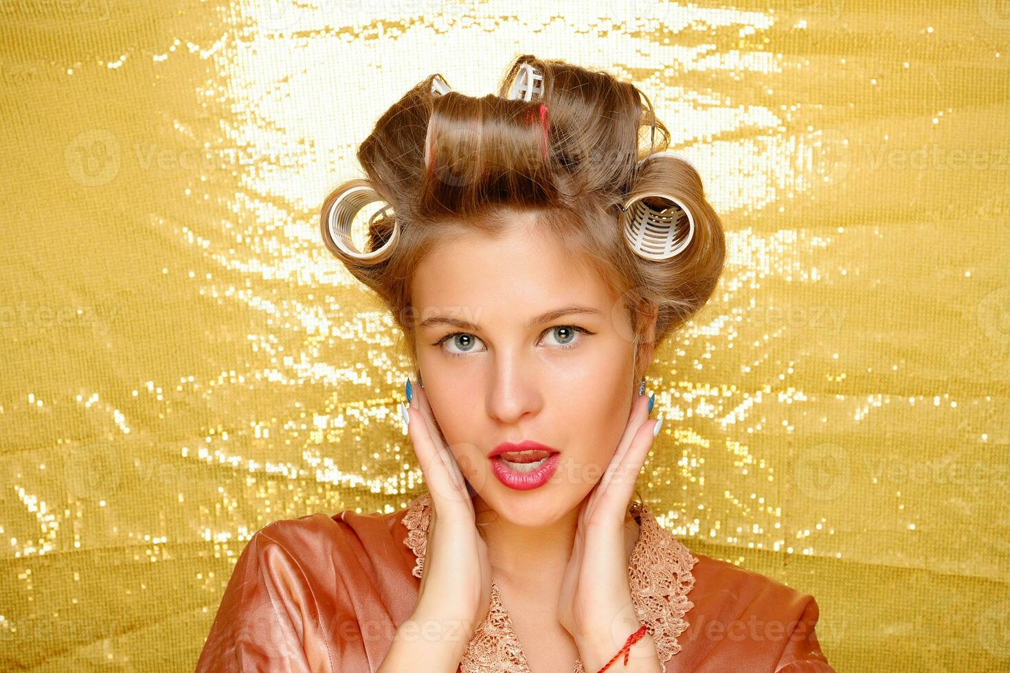 Beautiful girl in hair curlers isolated on gold photo