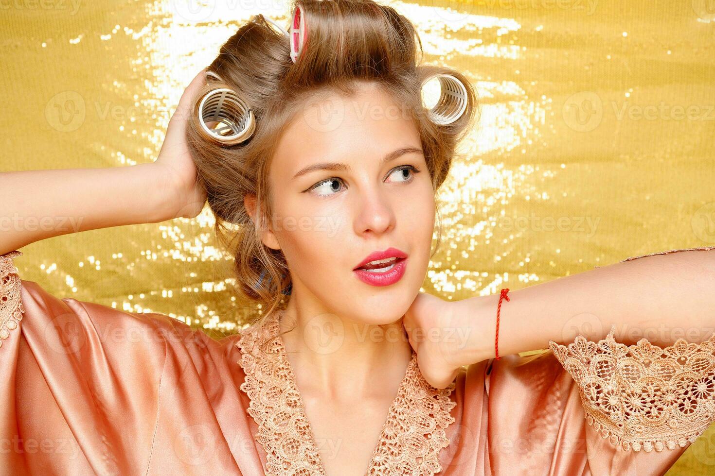 Beautiful girl in hair curlers isolated on gold photo