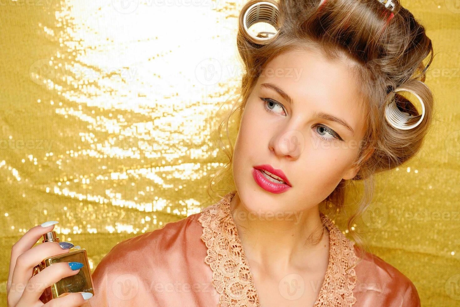 Beautiful girl in hair curlers isolated on gold photo