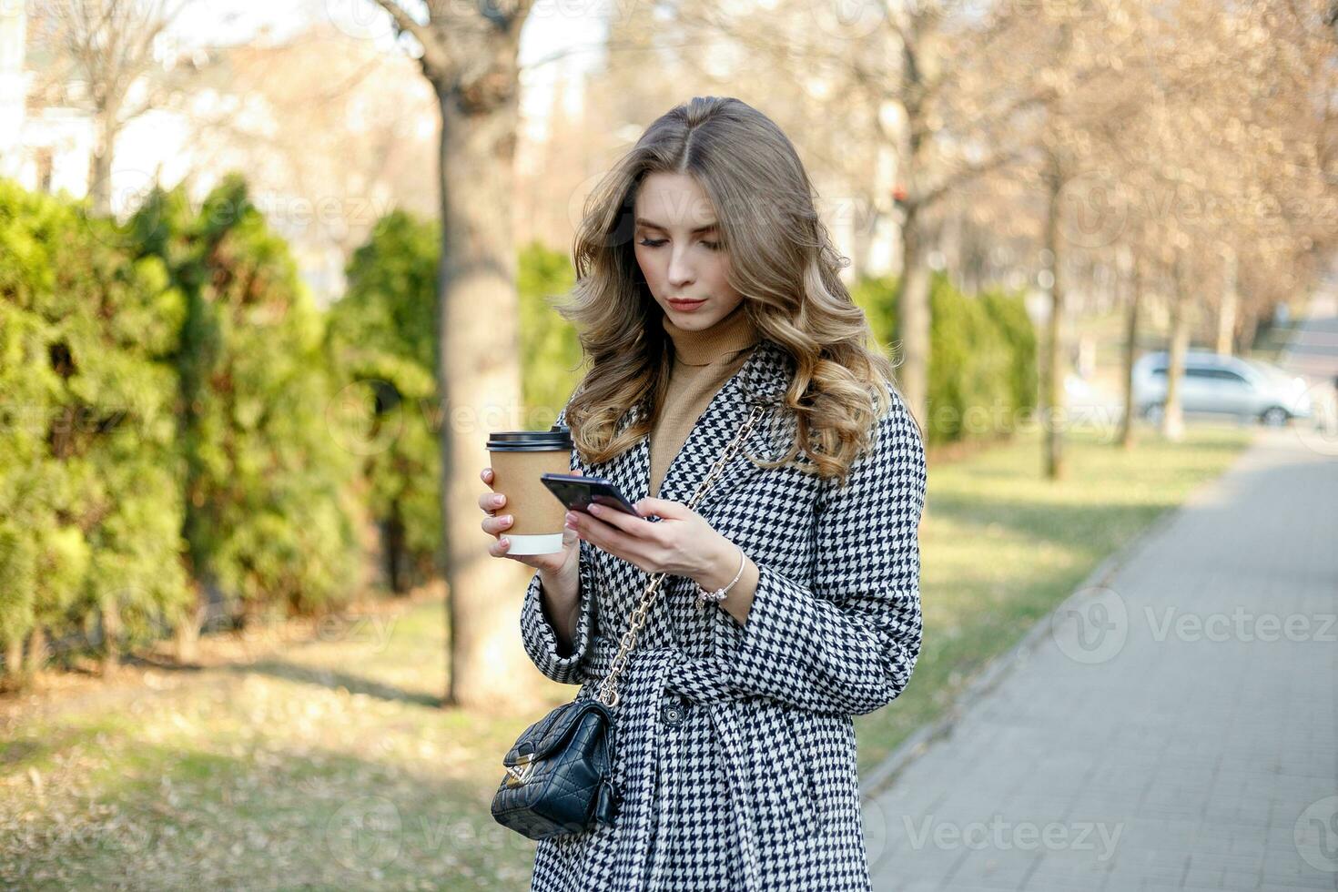 woman in trench coat walking and drinking coffee from paper cup photo