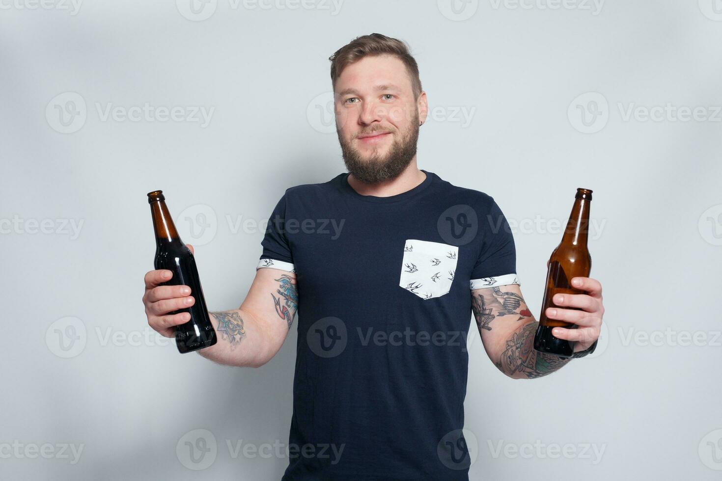 Brutal bearded male with tattooed arm drinks a beer from a bottle. photo