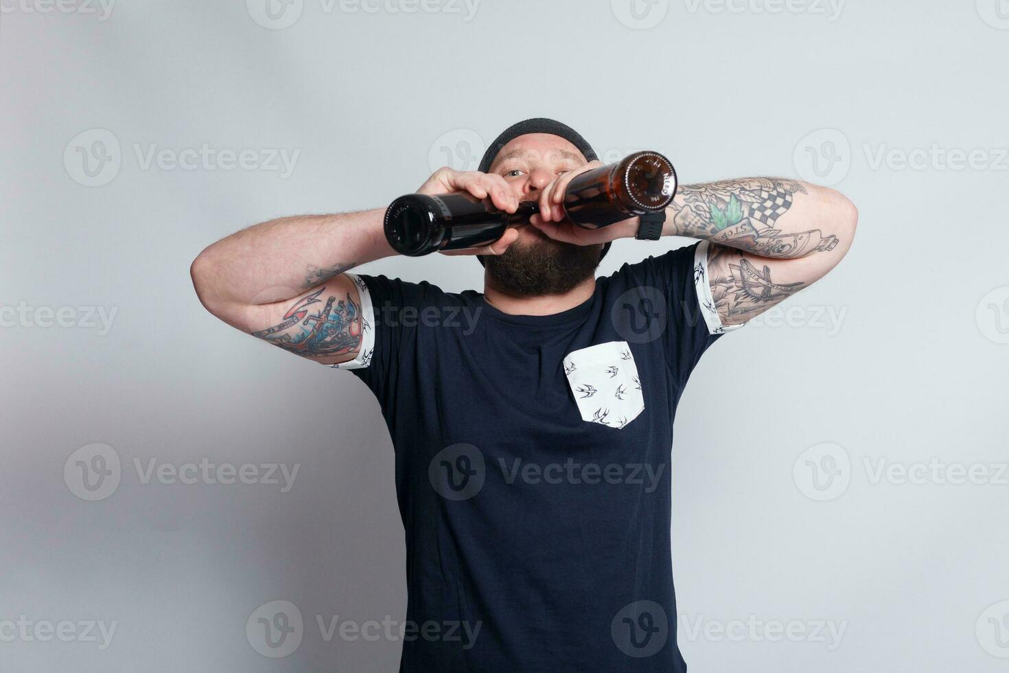 Brutal bearded male with tattooed arm drinks a beer from a bottle. photo