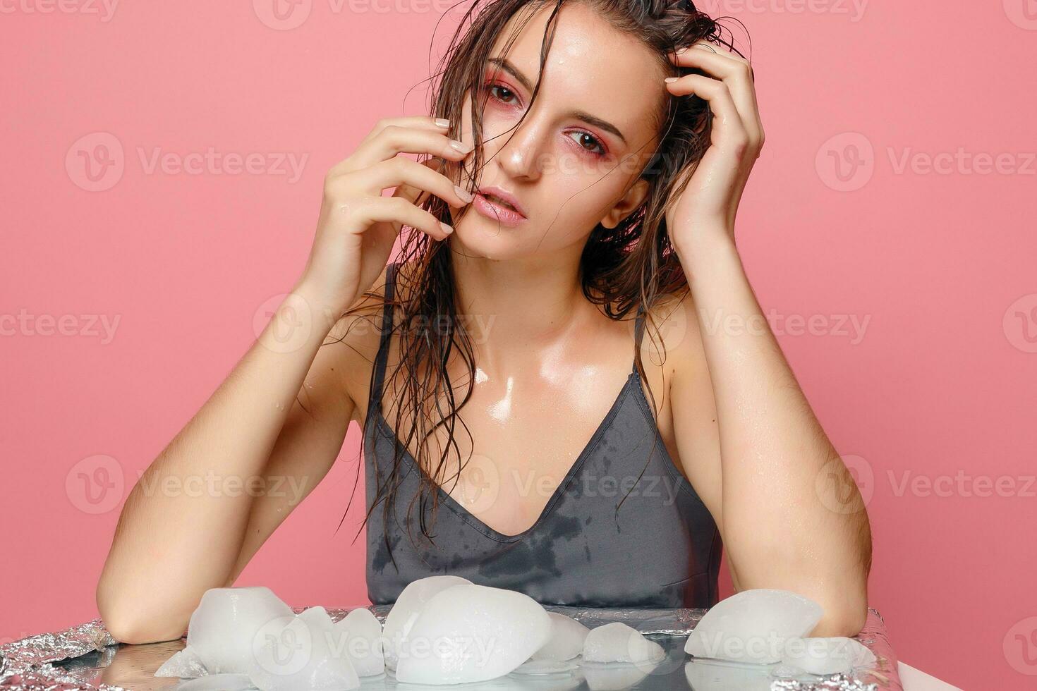 young woman applies the ice to face on a pink background. photo