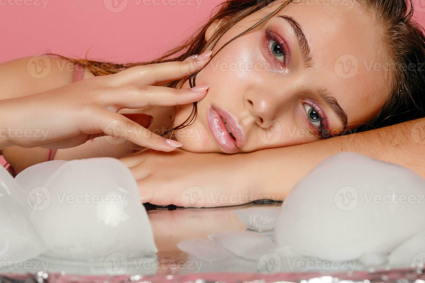 young woman applies the ice to face on a pink background. photo