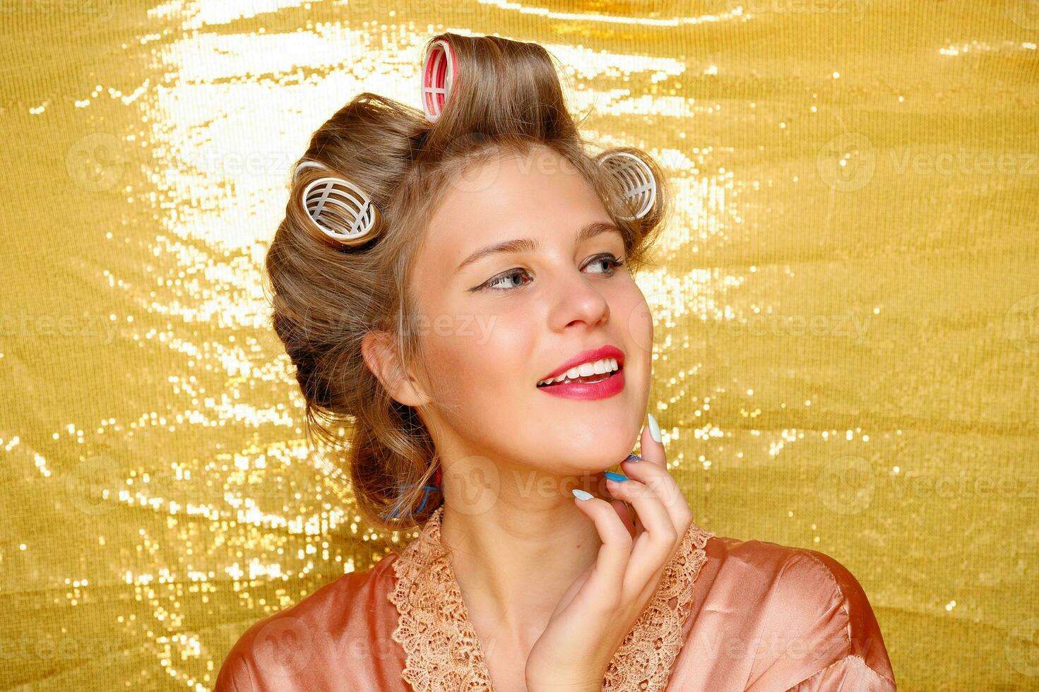 Beautiful girl in hair curlers isolated on gold photo