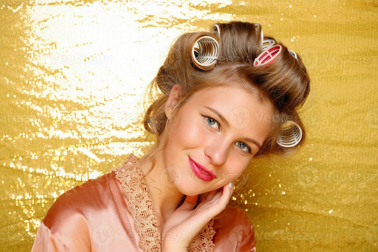 Beautiful girl in hair curlers isolated on gold photo