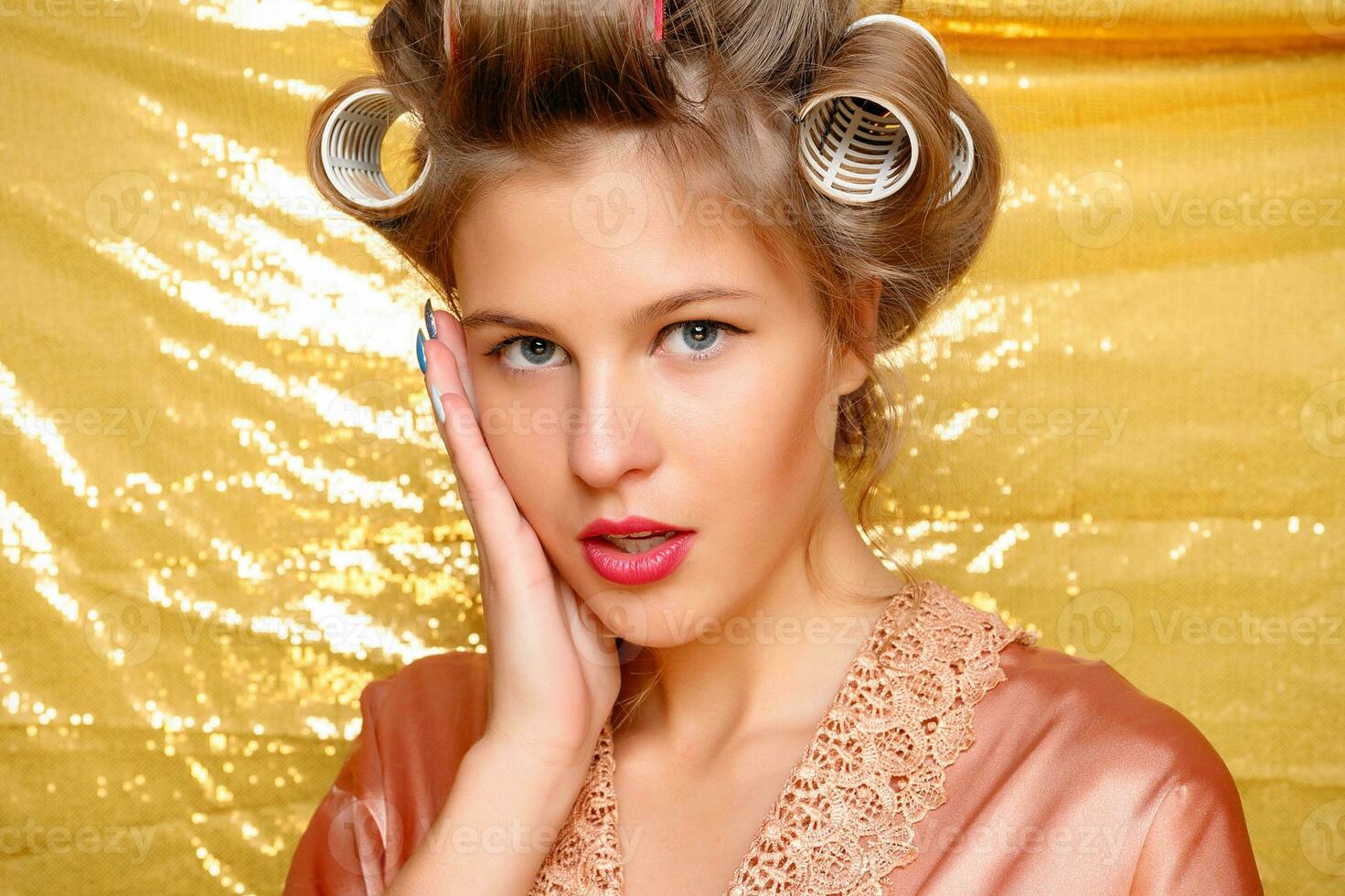 Beautiful girl in hair curlers isolated on gold photo