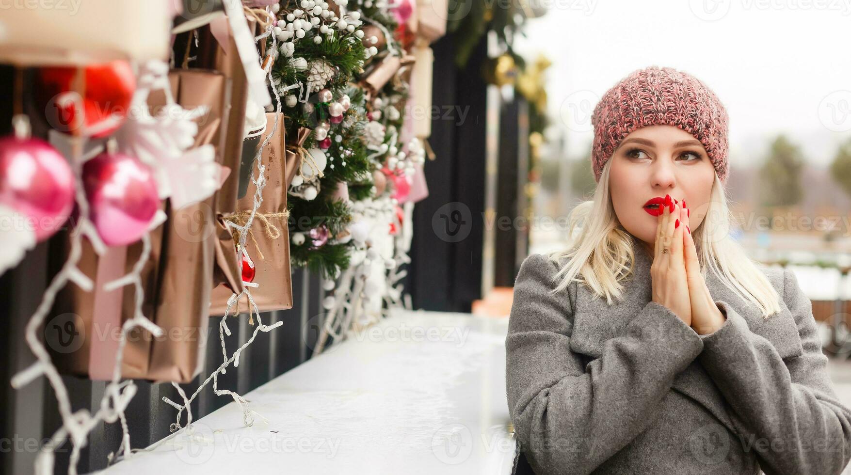 Gorgeous fashionable young blonde woman sitting near the window of the store or coffeehouse, dreaming, praying for a miracle before Christmas. cold winter day. photo