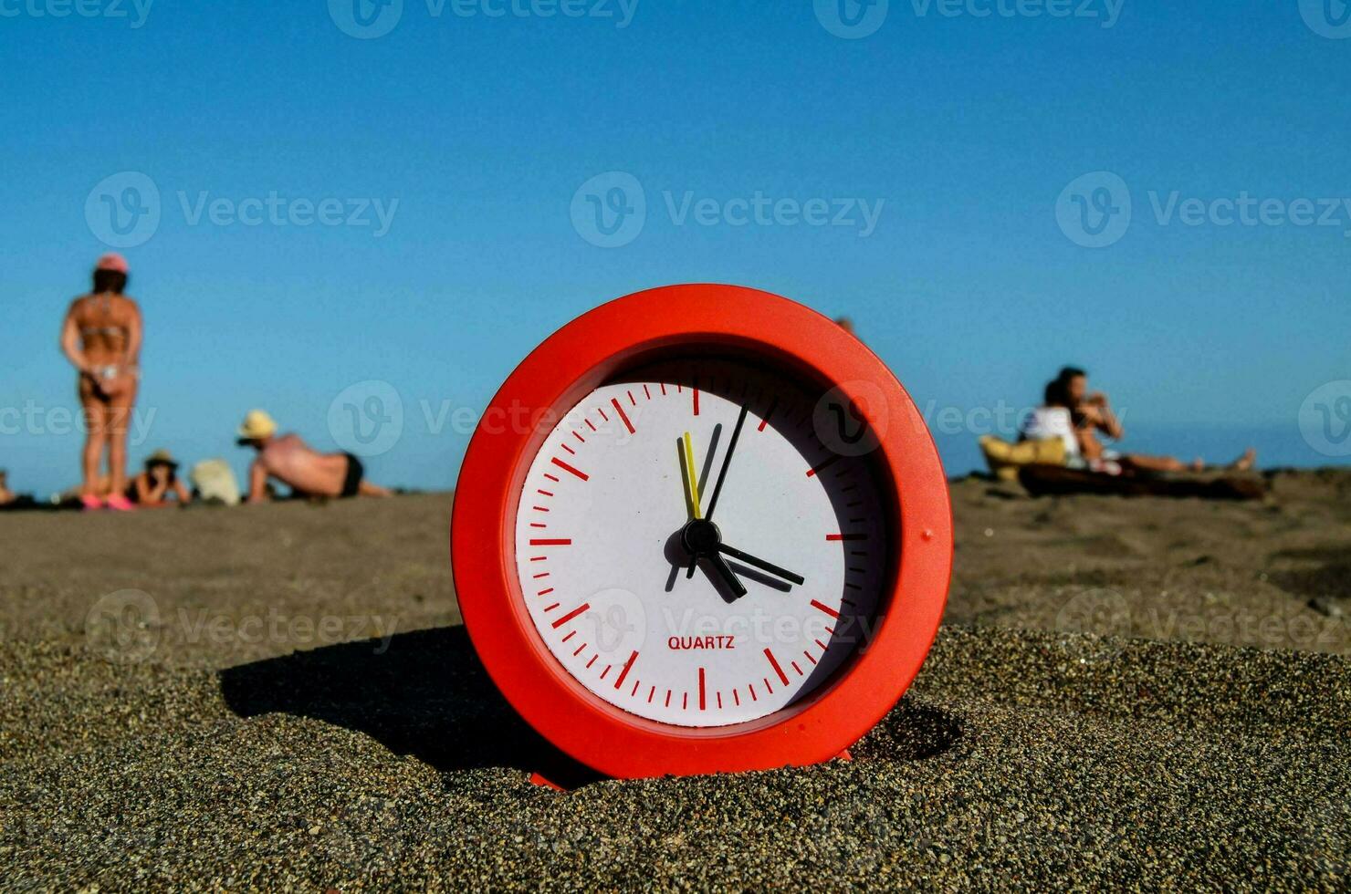 a red clock on the beach with people in the background photo