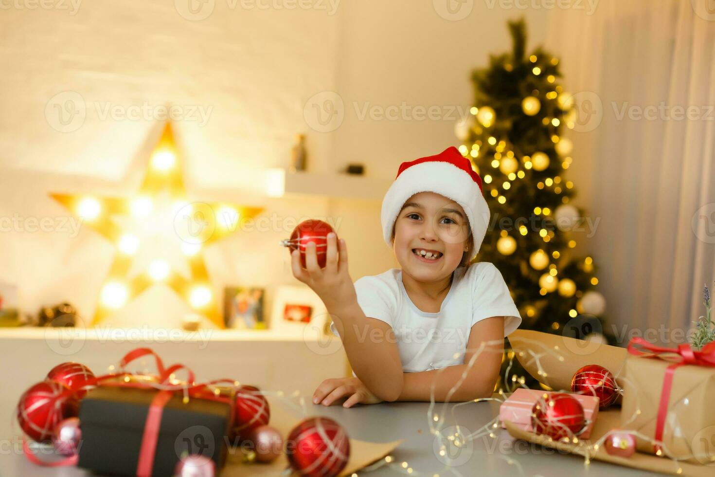 Portrait of a laughing preschool girl in Santa hat holding Christmas decoration in hands photo