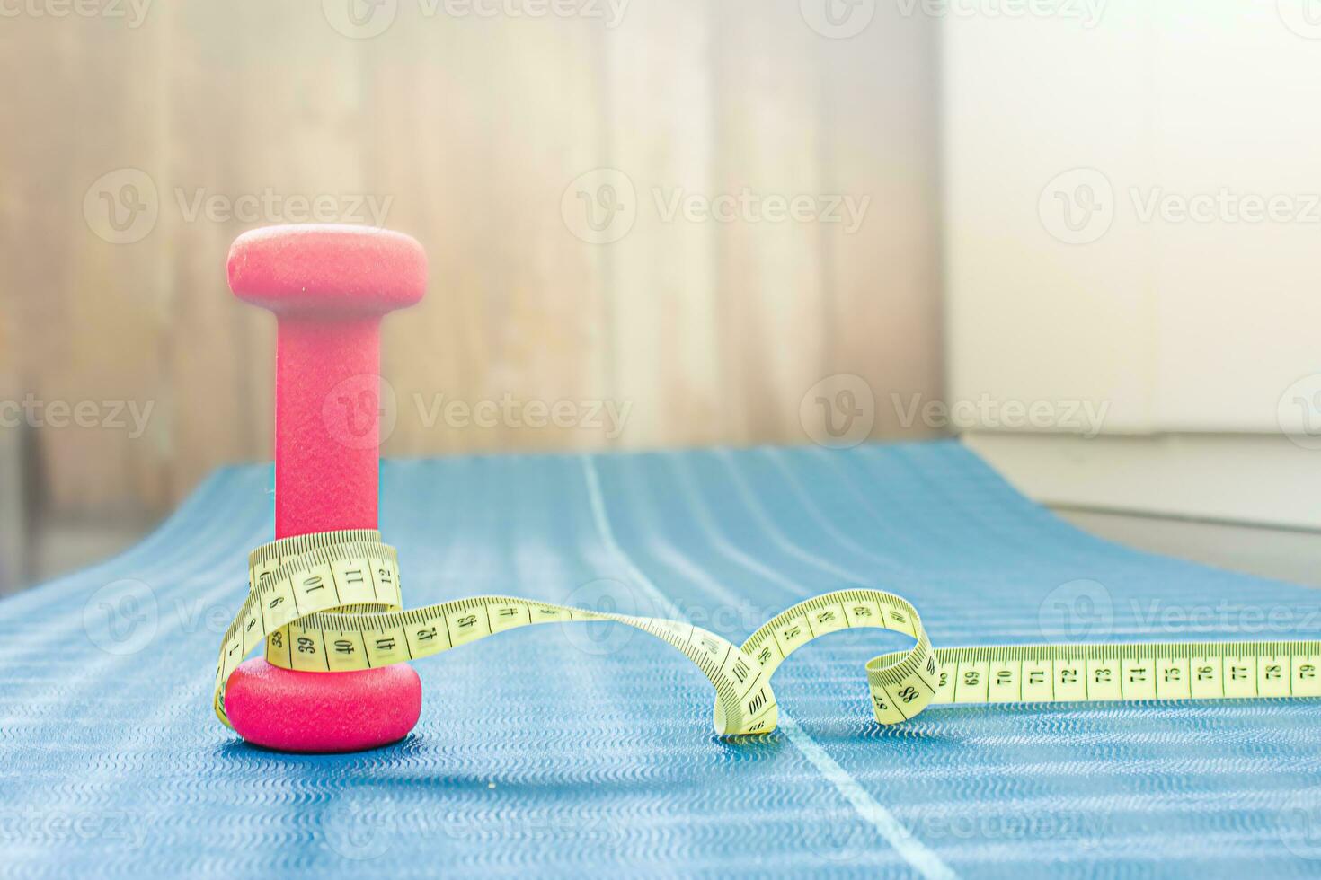 Centimeter tape around a dumbbell on a yoga mat. Weight loss concept photo