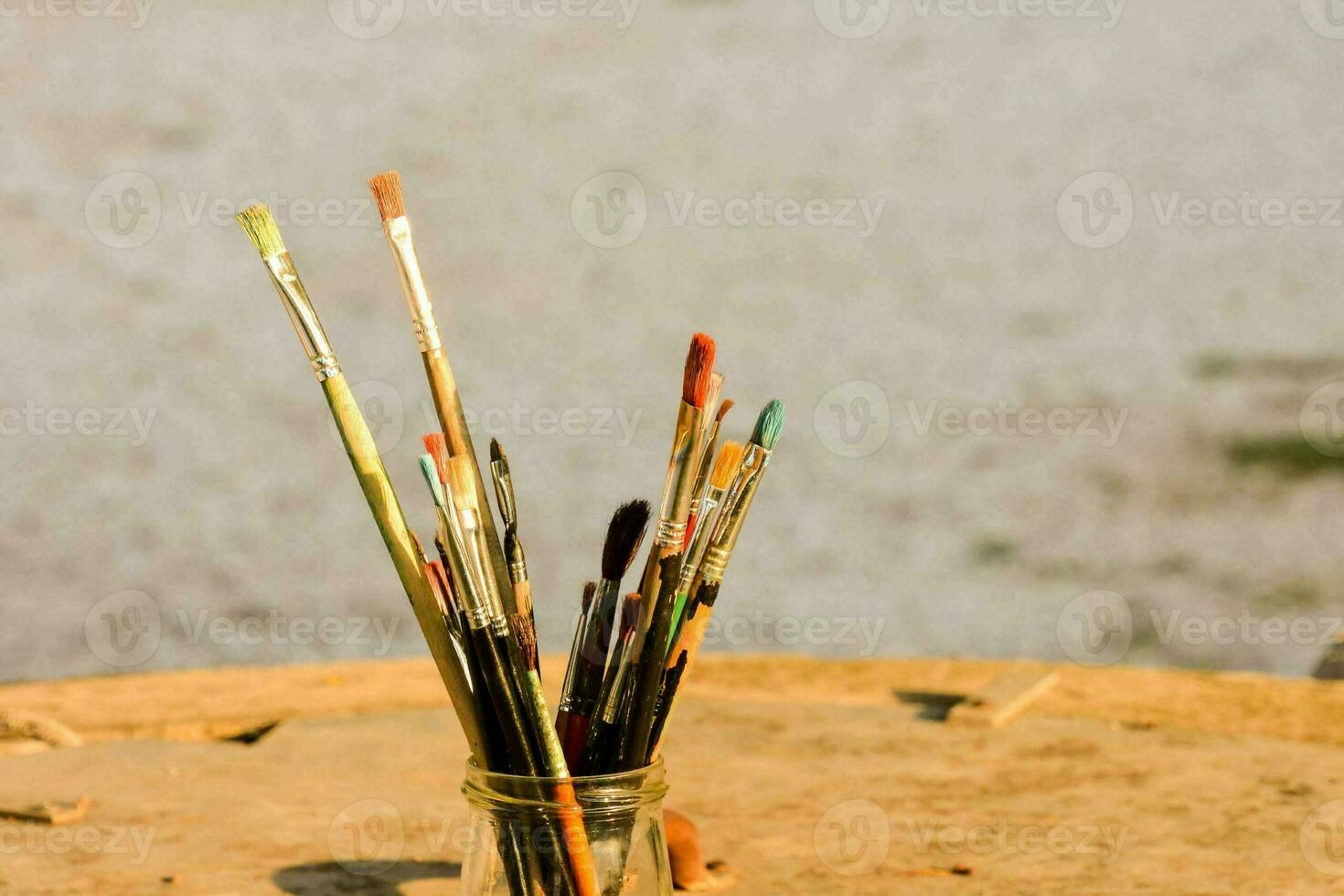 a vase filled with paint brushes on a table photo