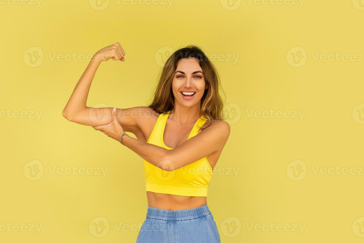 Studio photo of pretty brunette woman in sportive outfit posing on yellow background.