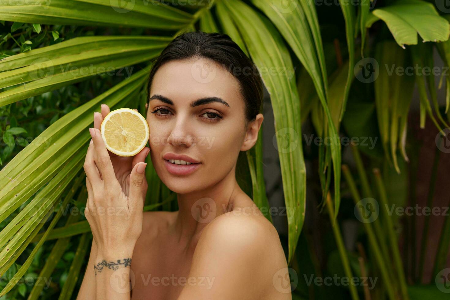 Beautiful woman holds lemons. Photo of attractive woman with perfect makeup on   green palm trees  background. Beauty concept