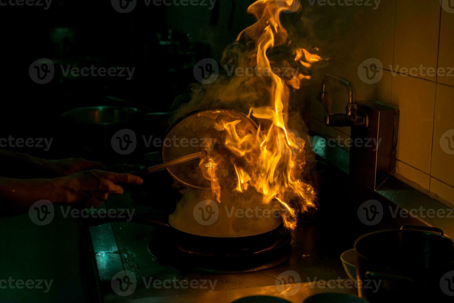 Chef cooking and doing flambe on food in restaurant kitchen photo