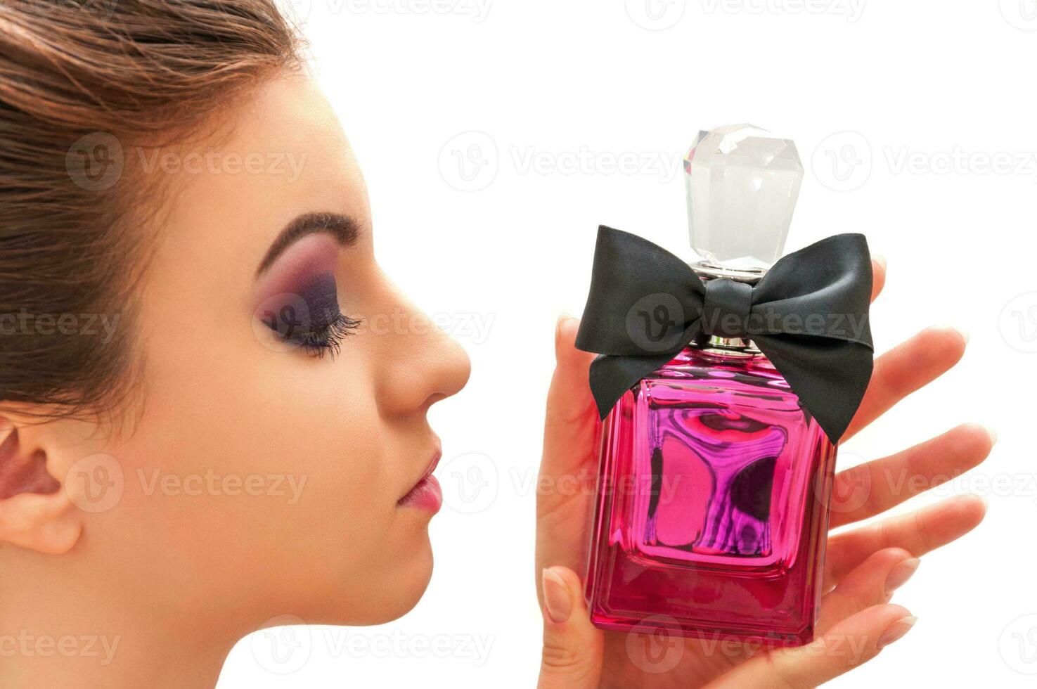 Close up shot of the young model with professional make up looking at pink bottle with parfum photo