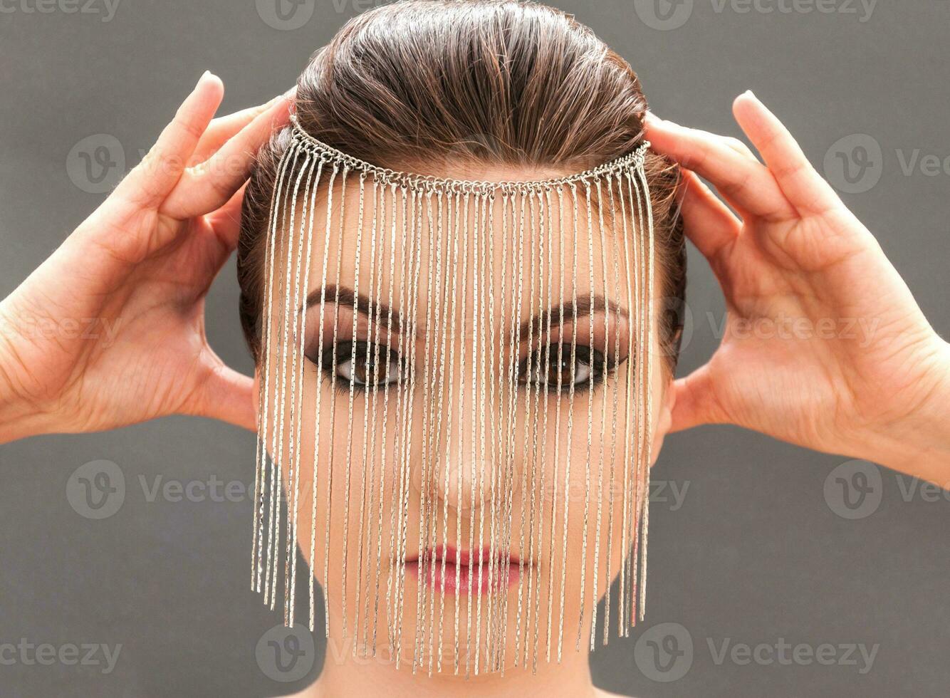 Young model with professional make up closing her face with metal mask photo