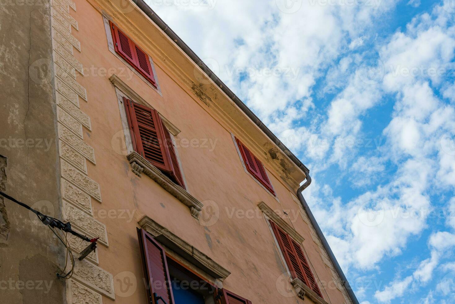 Unusual look at the old italian building with closed window shutters and blue cloudy sky on the background photo