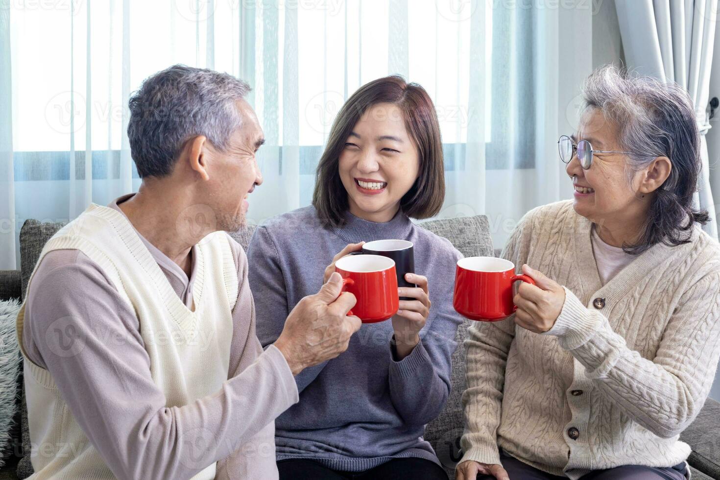 Asian family of senior father mother and daughter sitting on couch with happy smile in retirement home drinking hot tea to celebrate their holiday together for elder care and spending valuable time photo