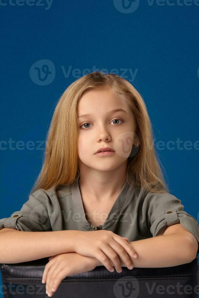 Little girl with gray eyes and blond hair sits on a chair photo