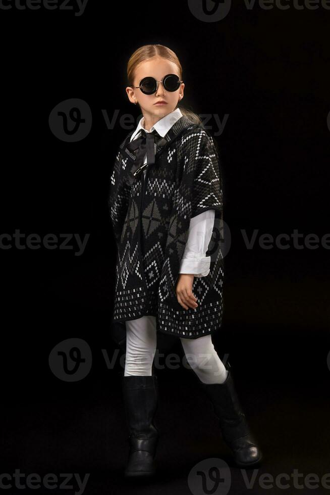 Little girl in a black glasses, dark poncho, black boots and a clutch in her hand photo