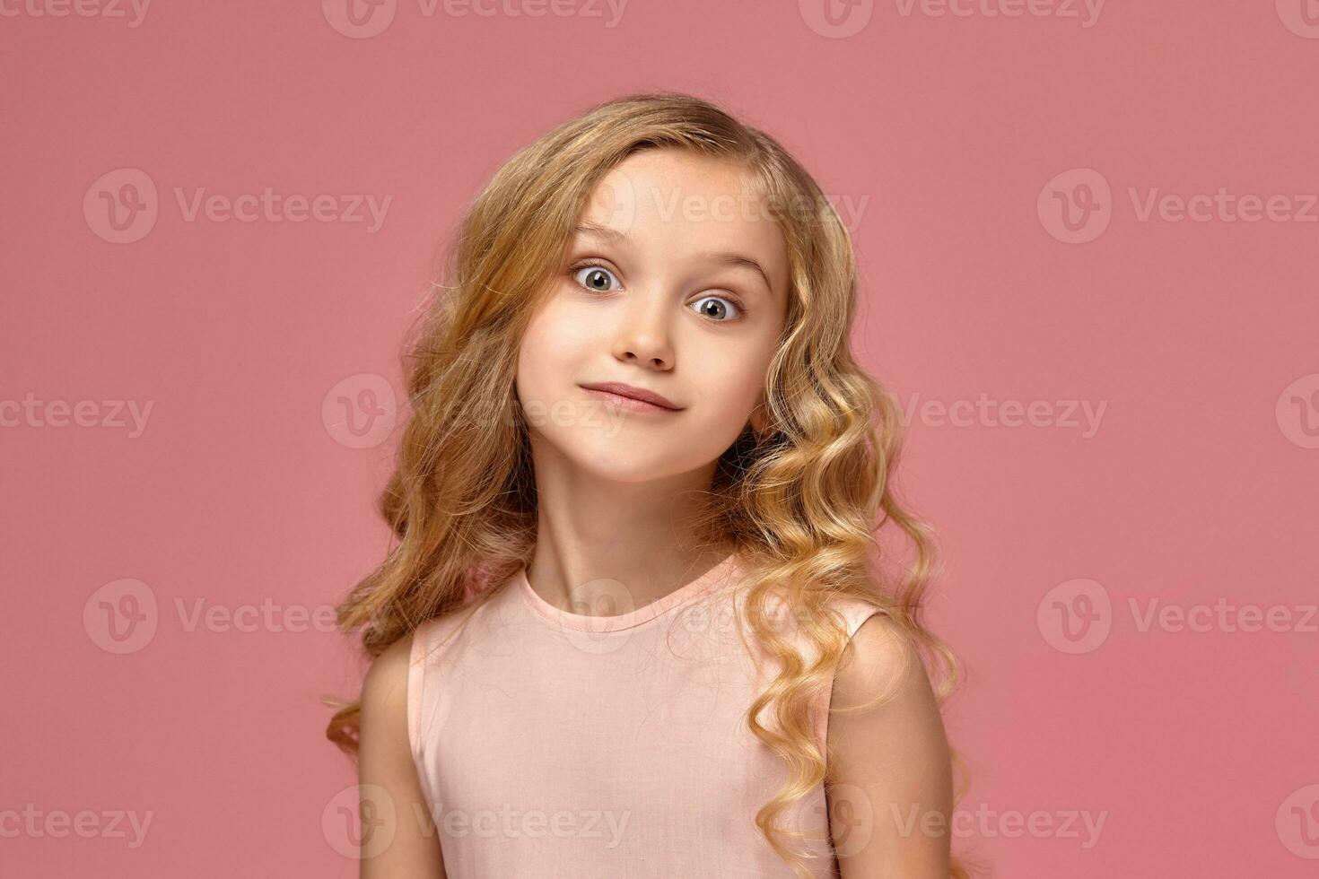 Little girl with a blond curly hair, in a pink dress is posing for the camera photo