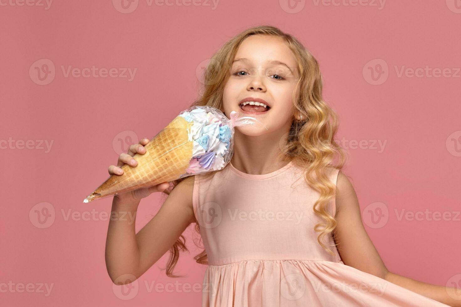 Little girl with a blond curly hair, in a pink dress is posing with an ice-cream photo