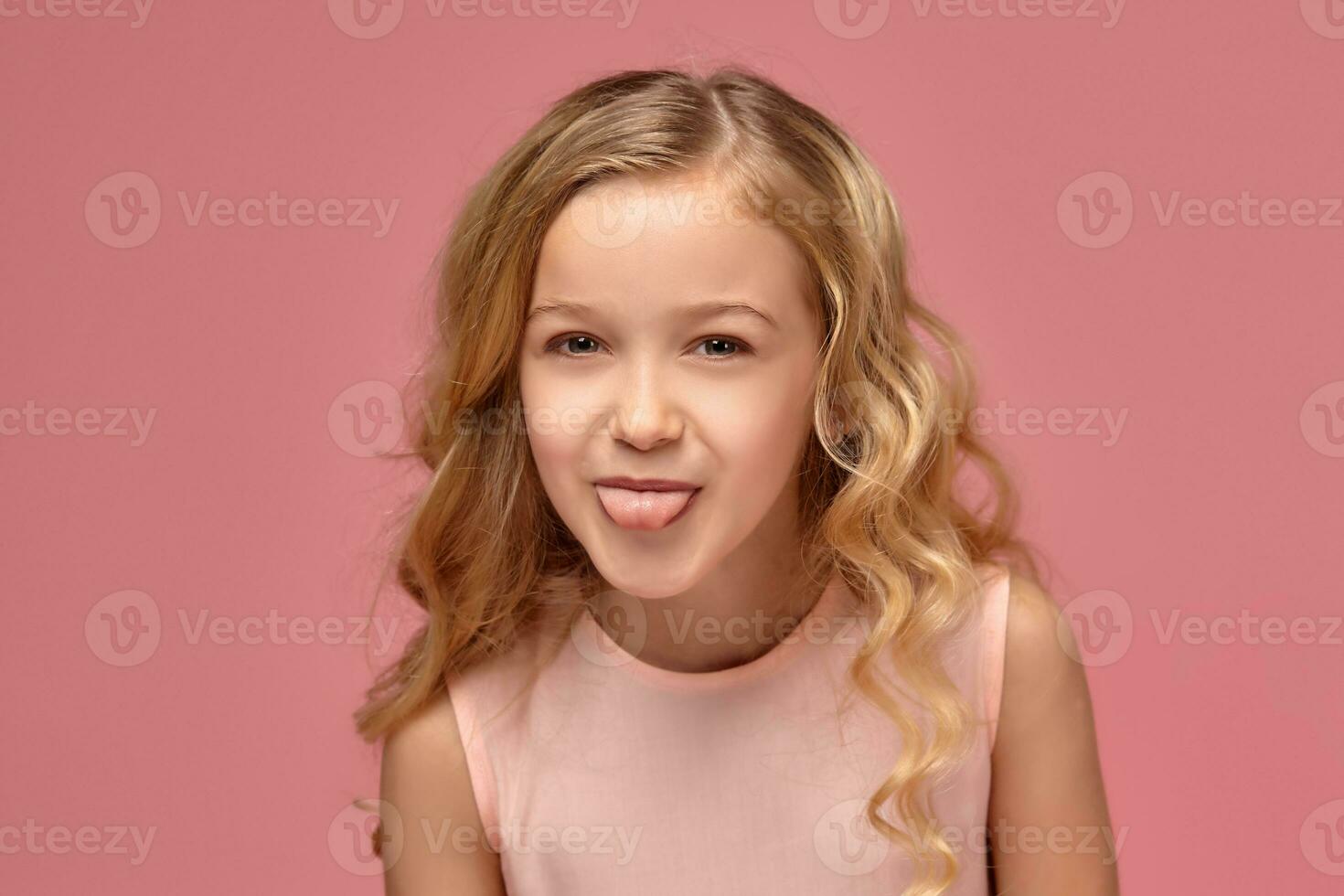 Little girl with a blond curly hair, in a pink dress is posing for the camera photo