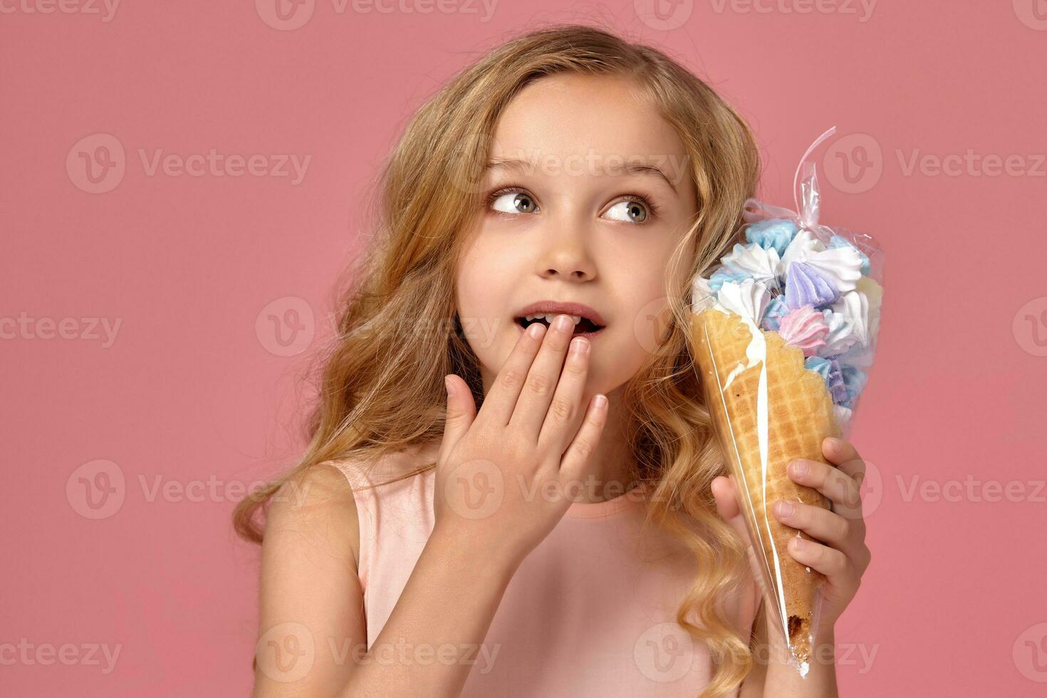 Little girl with a blond curly hair, in a pink dress is posing with an ice-cream photo