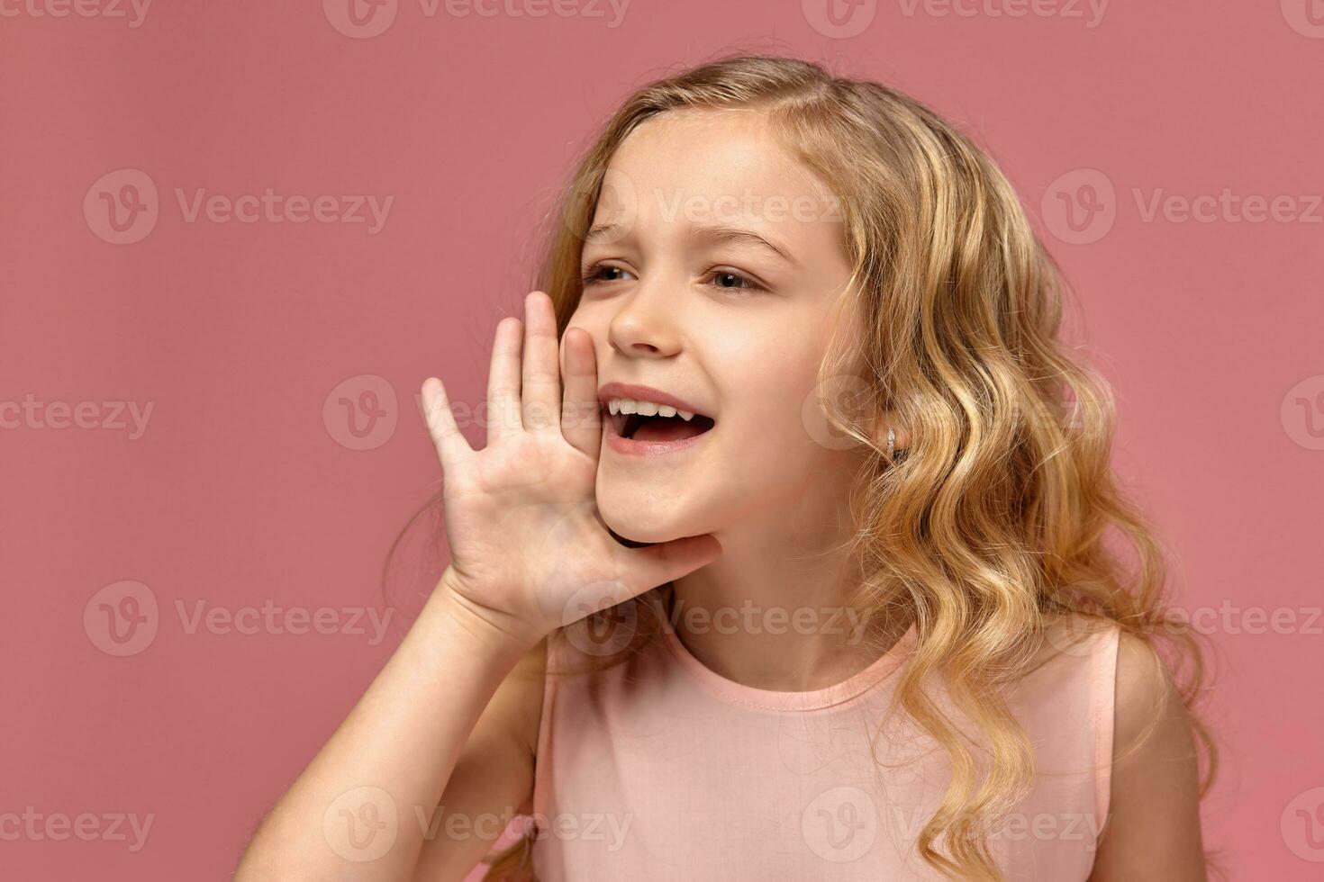 Little girl with a blond curly hair, in a pink dress is posing for the camera photo