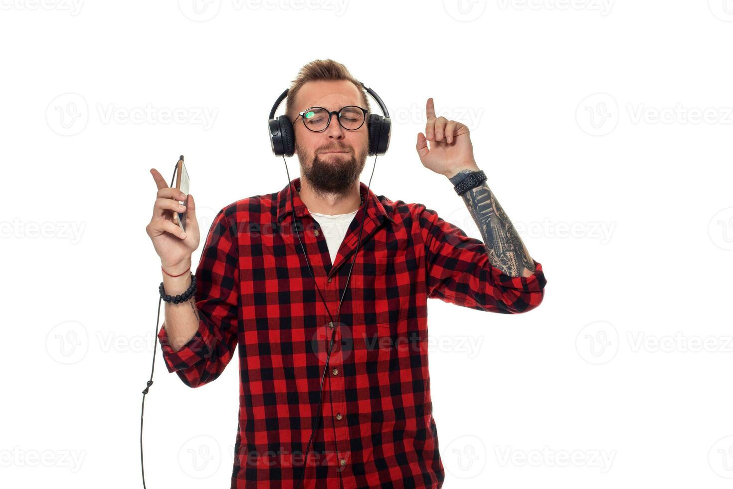 Young hipster man in checkered shirt and glasses wearing earphones looking happy on white background. photo