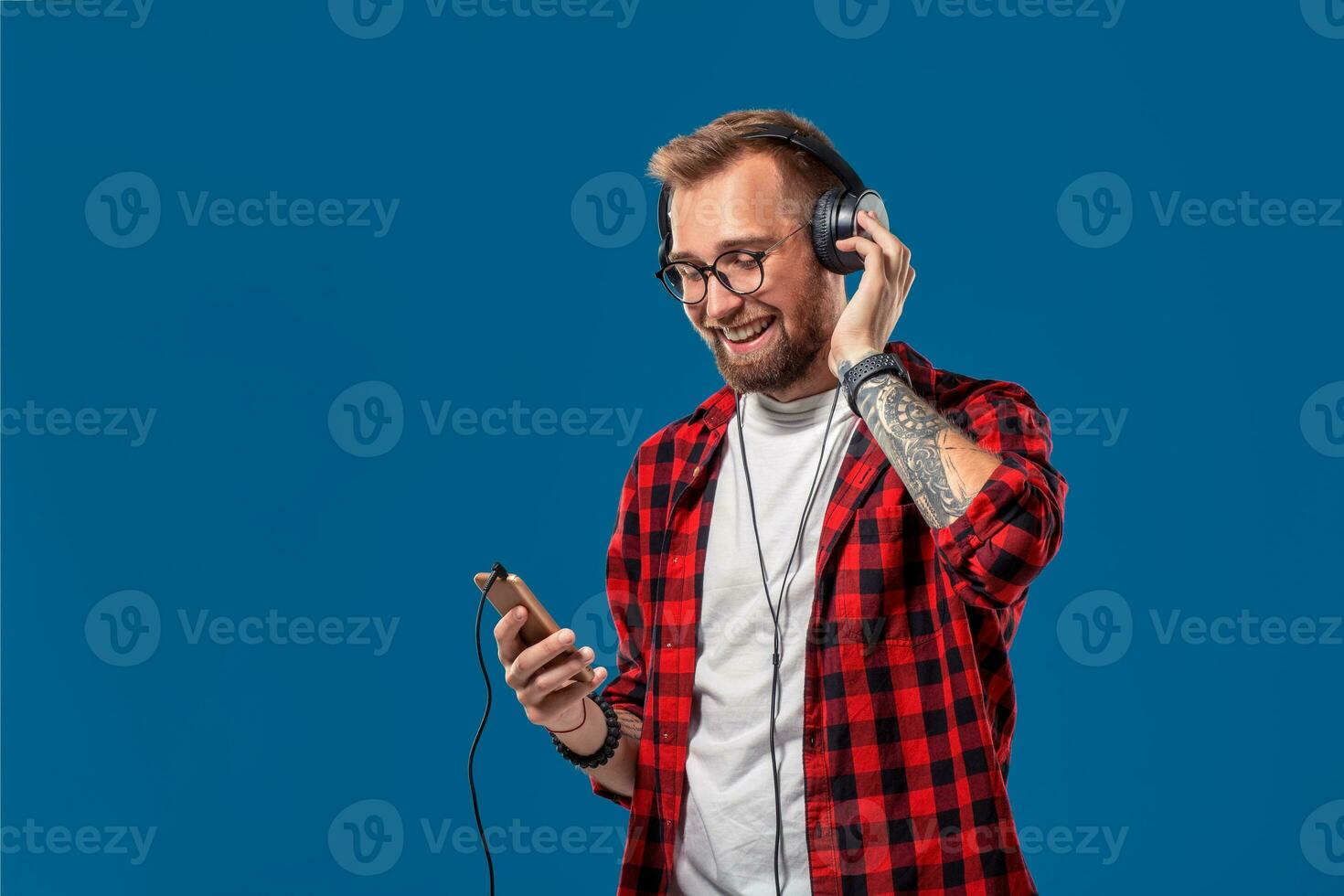 Happy young man listening to music with headphones. Handsome smiling guy in checkered shirt dancing with headphones. photo