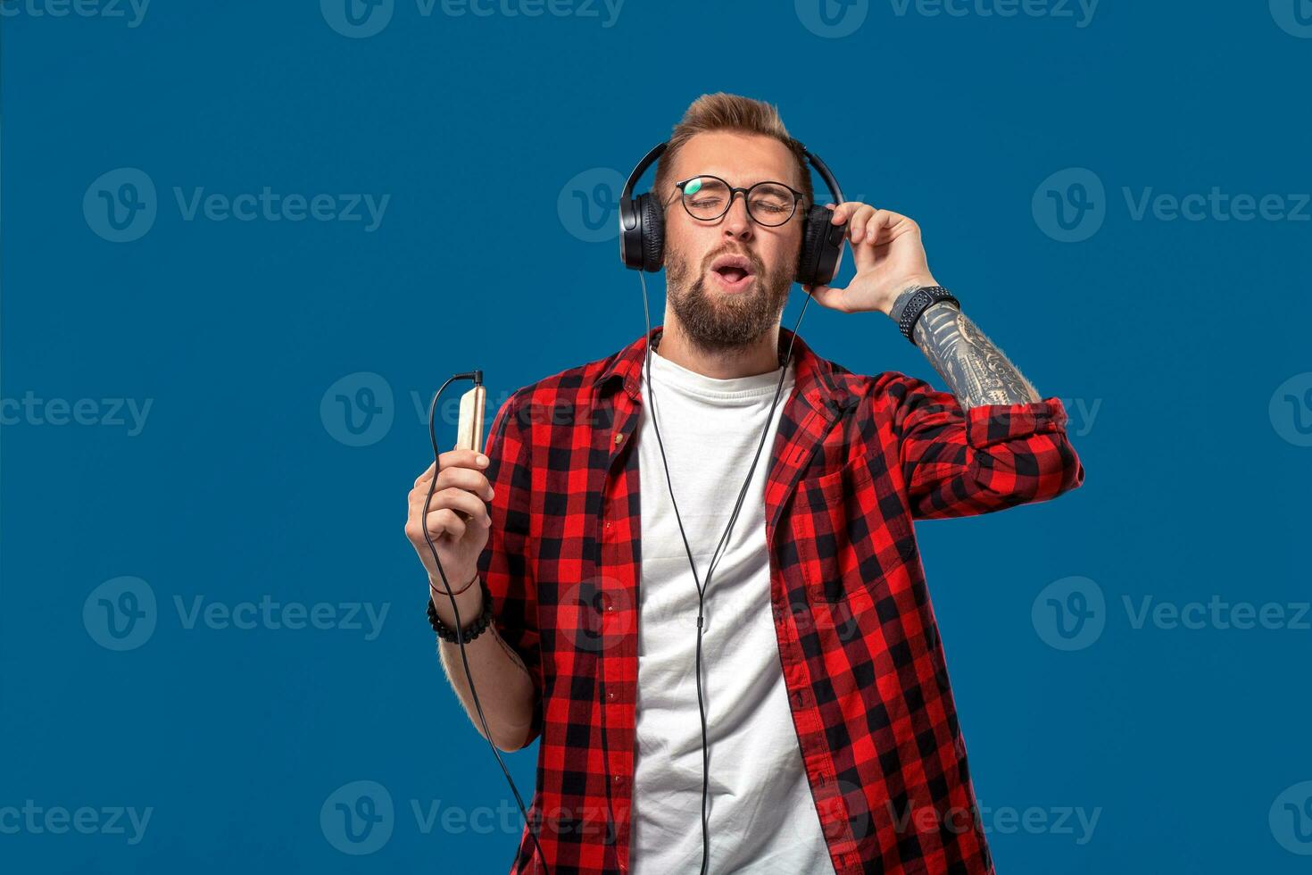 Happy young man listening to music with headphones. Handsome smiling guy in checkered shirt with closed eyes dancing with headphones. photo