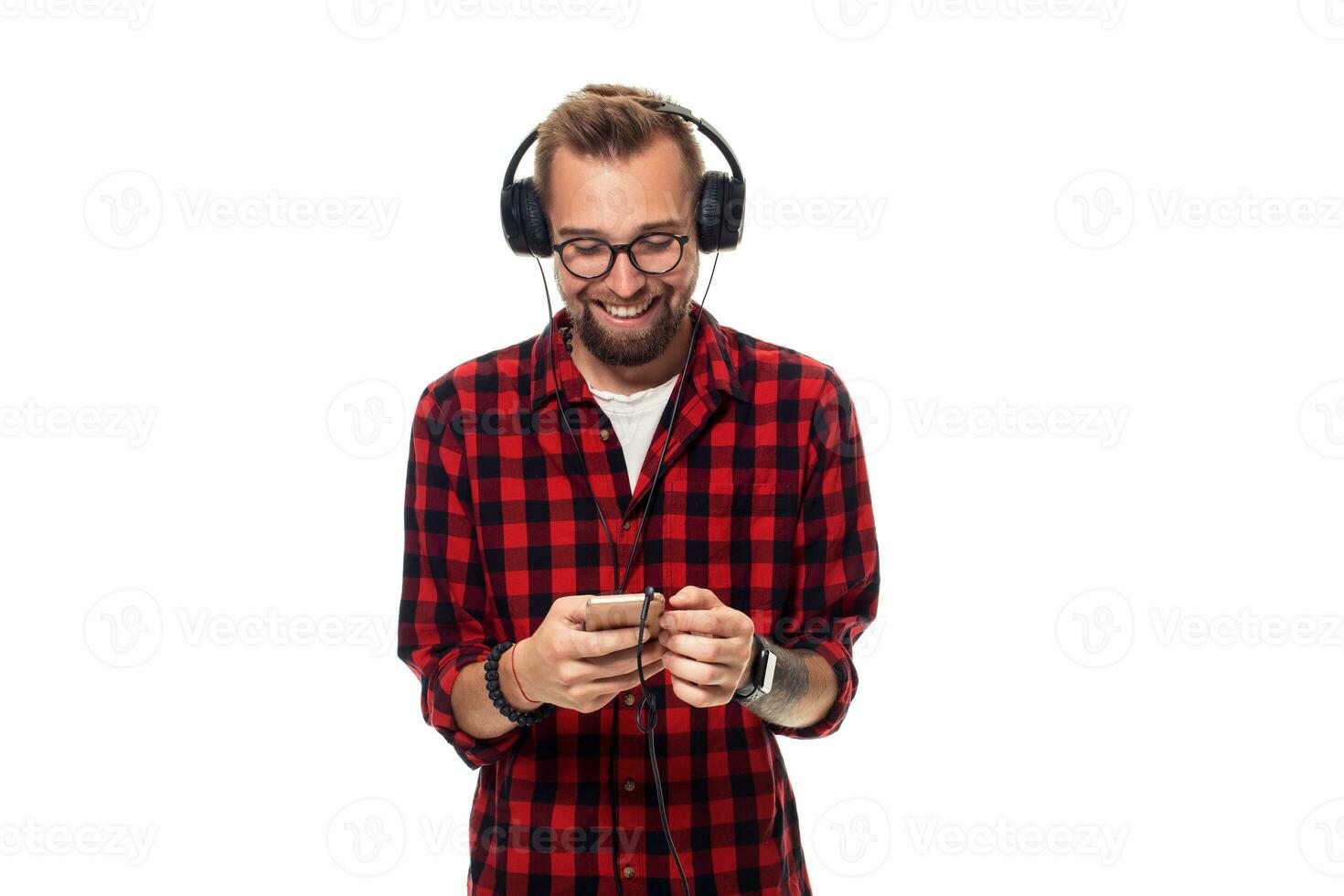 joven hipster hombre en a cuadros camisa y lentes vistiendo auriculares mirando contento en blanco antecedentes. foto