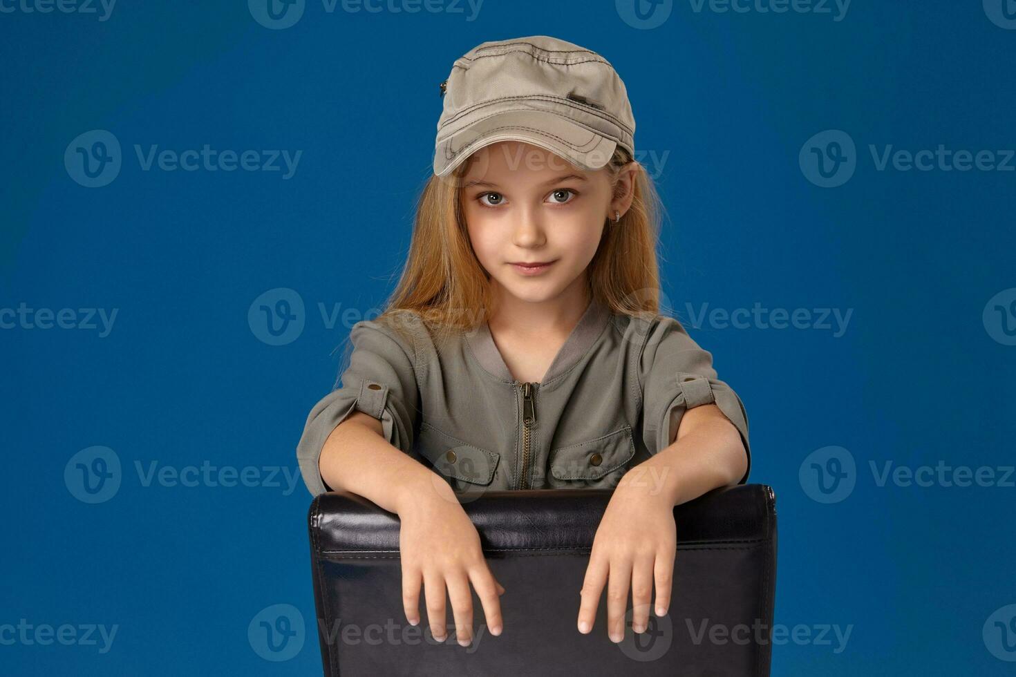 Little girl in a cap with gray eyes and blond hair sitting on a chair photo