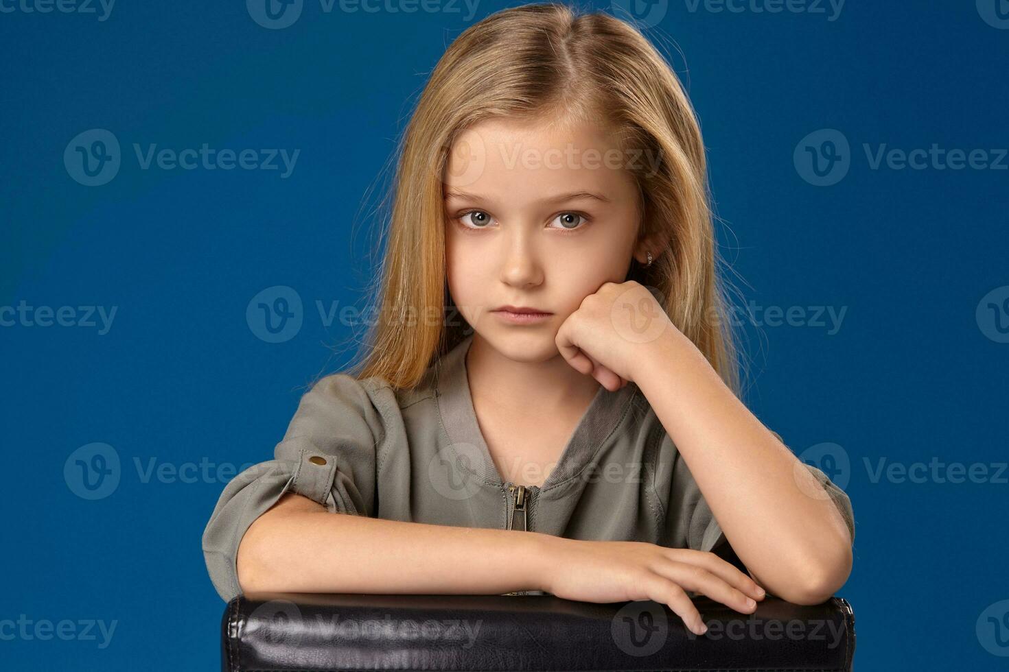 Little girl with gray eyes and blond hair sits on a chair photo