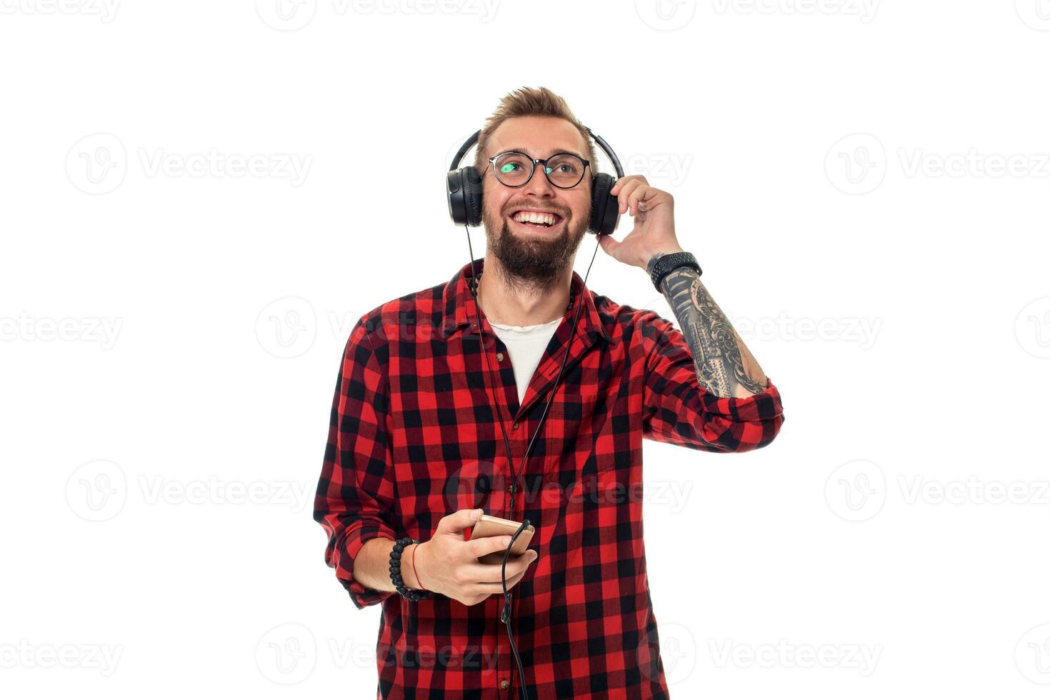 joven hipster hombre en a cuadros camisa y lentes vistiendo auriculares mirando contento en blanco antecedentes. foto