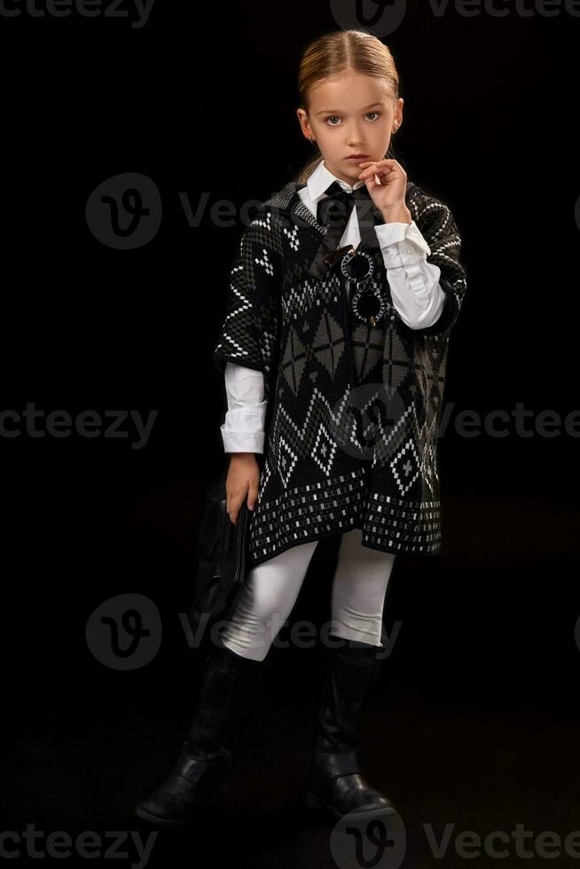 Little girl in a dark poncho, black boots and a clutch in her hand photo