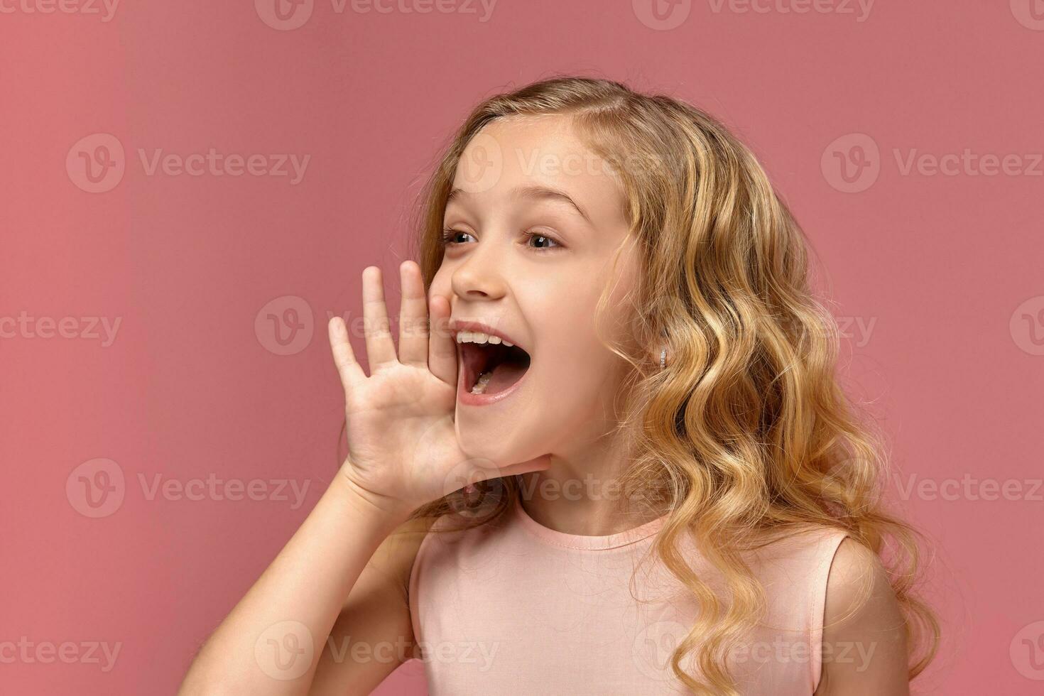 Little girl with a blond curly hair, in a pink dress is posing for the camera photo