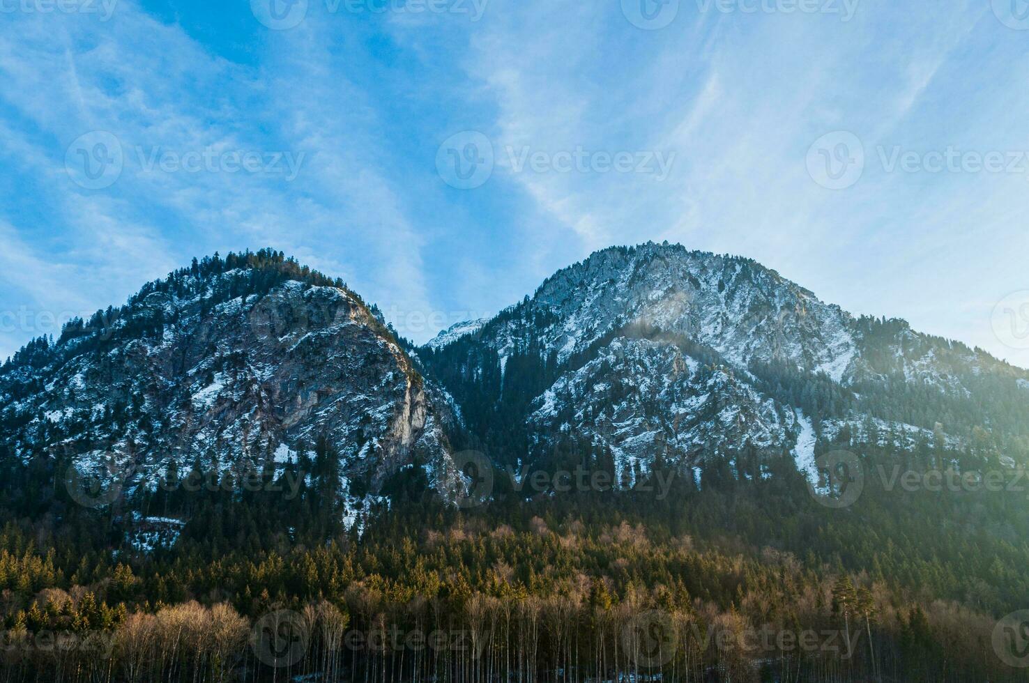 Two mountains covered with snow during the sunset with a small green forest at the bottom photo