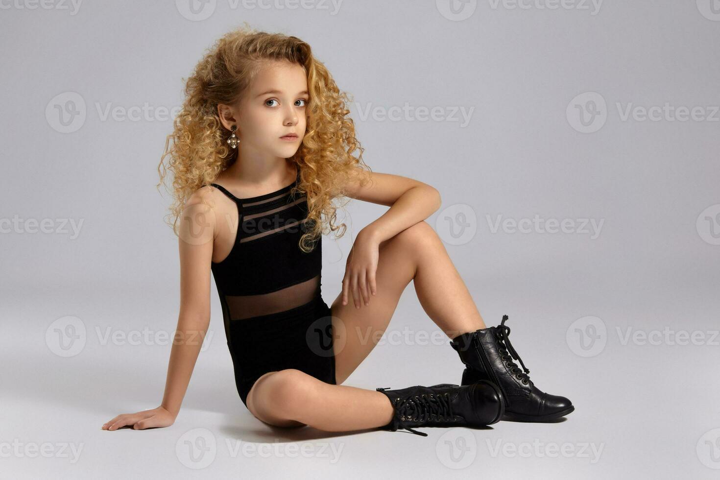 Beautiful little girl gymnast in a black sports swimsuit and boots on a gray background. photo