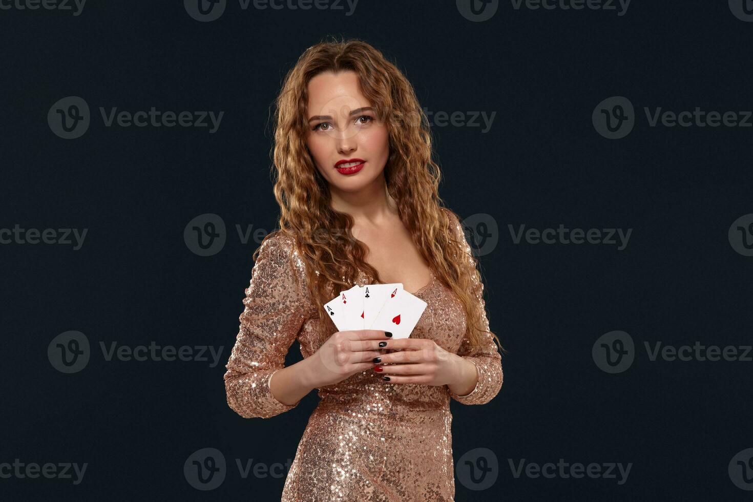 Beautiful young emotional woman in cocktail dress showing her cards to opponent, four of aces, best hand. Blcak background, studio shot photo