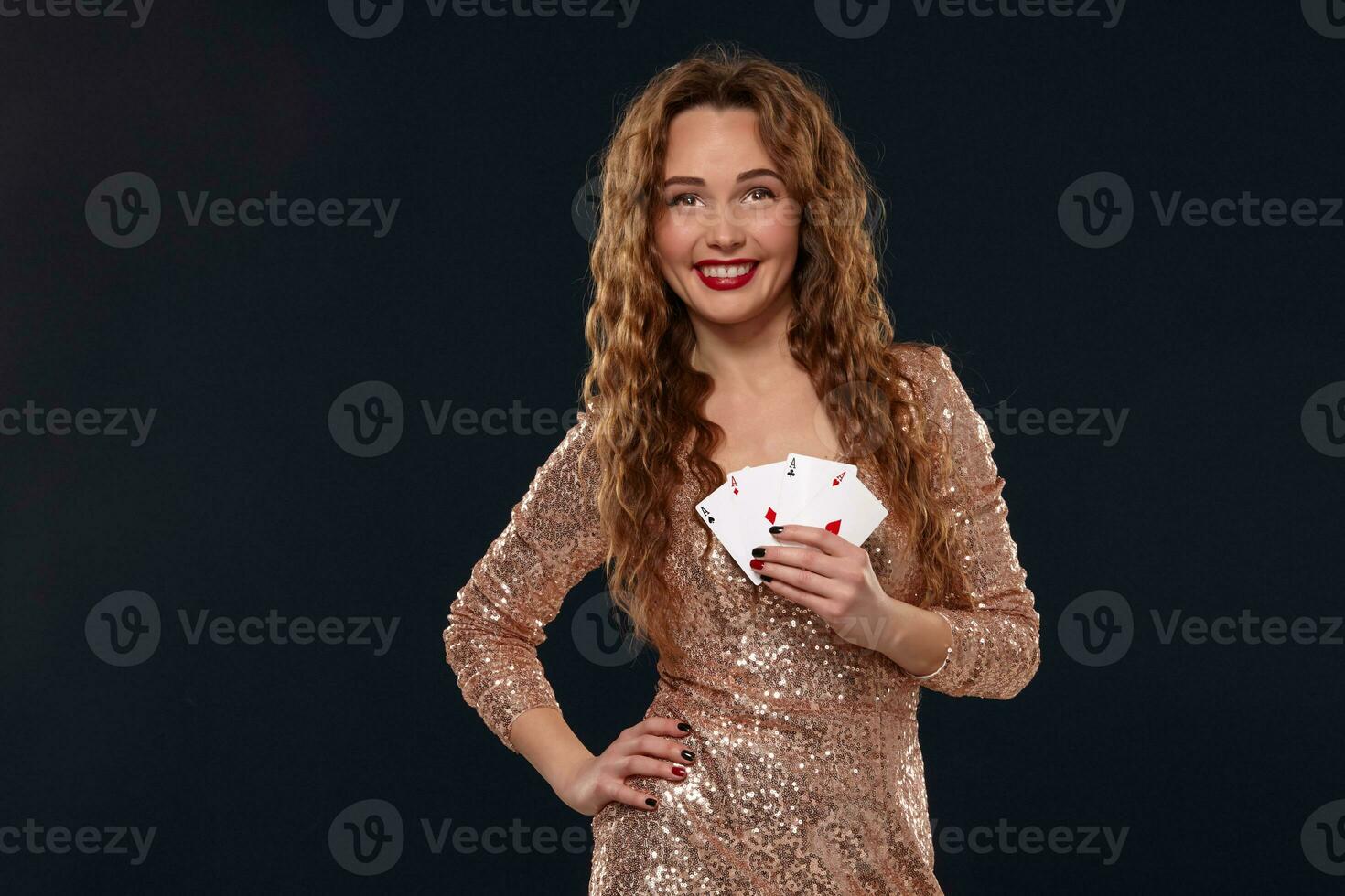 Beautiful young emotional woman in cocktail dress showing her cards to opponent, four of aces, best hand. Blcak background, studio shot photo