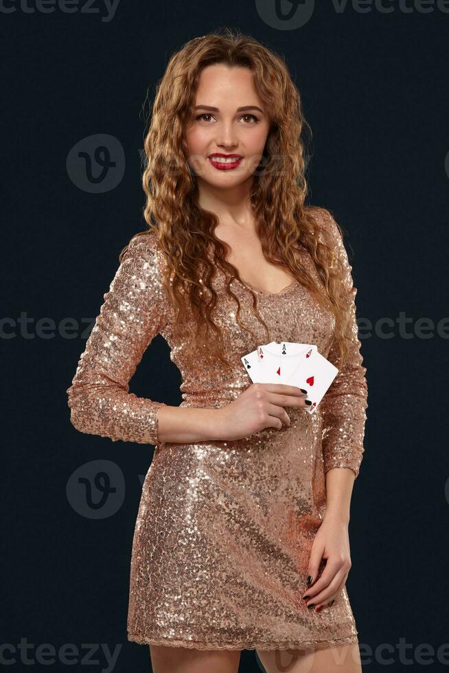 Beautiful young emotional woman in cocktail dress showing her cards to opponent, four of aces, best hand. Blcak background, studio shot photo