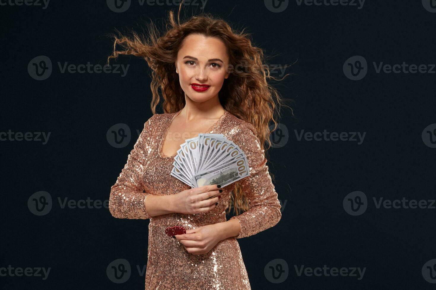 Image of lucky happy woman with brown long hair with fan of 100 dollar bills, lots of cash money, over black background photo